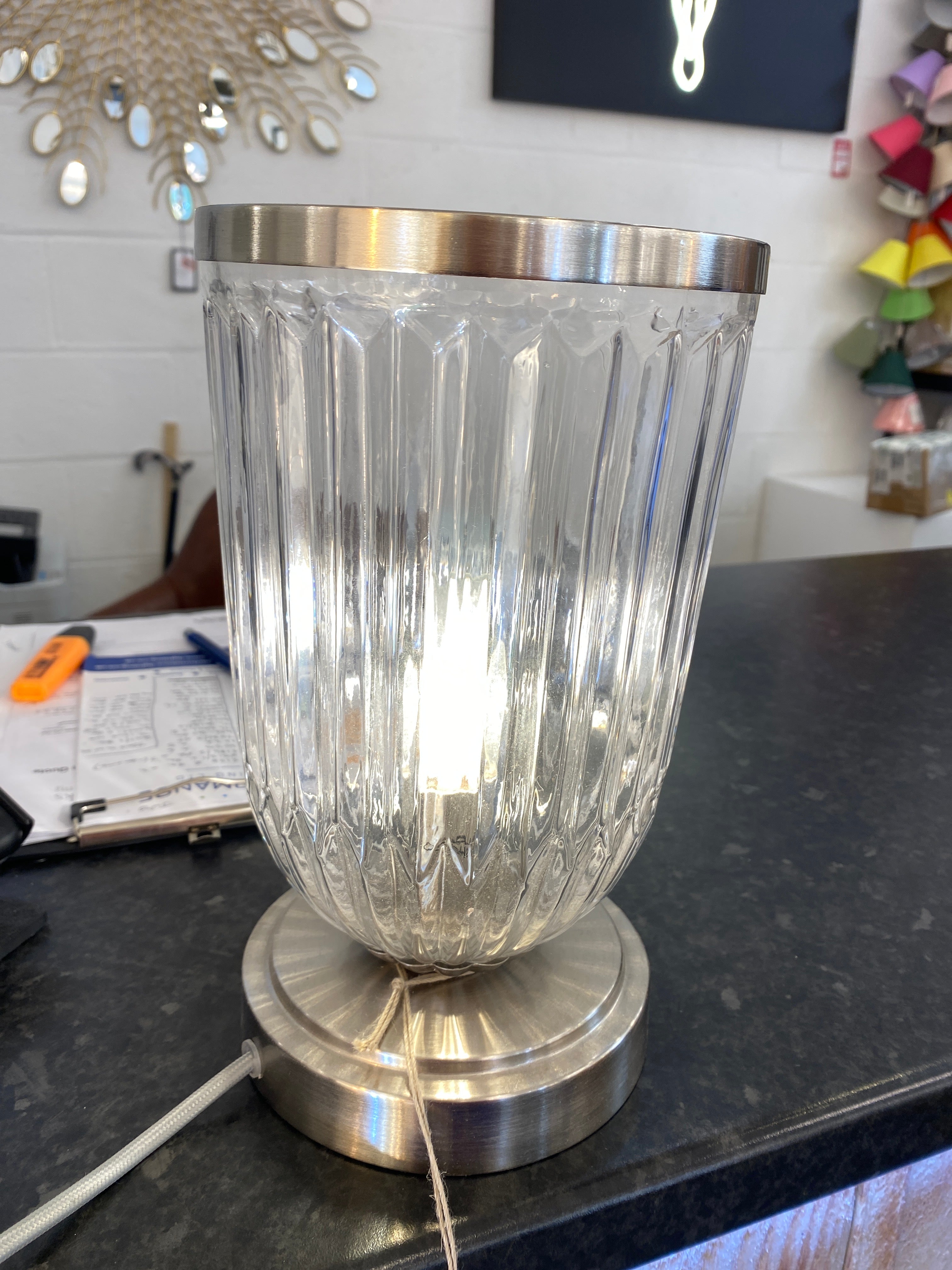 Clear glass light fixture with metallic base on a shop counter